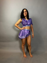 Woman with curly dark hair poses barefoot against a plain gray background, wearing a lavender purple Sequin Dance Costume featuring high waist shorts with half skirt and crop top in 4-way stretch mesh, perfect as a fire dancer outfit.