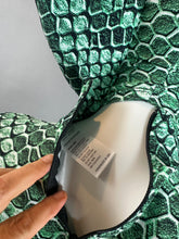 A hand opens the zipper of a green, scale-print fabric—part of the Green pixel Cobra Costume Snake Print Catsuit Serpent Cosplay—revealing a white tag with text inside.