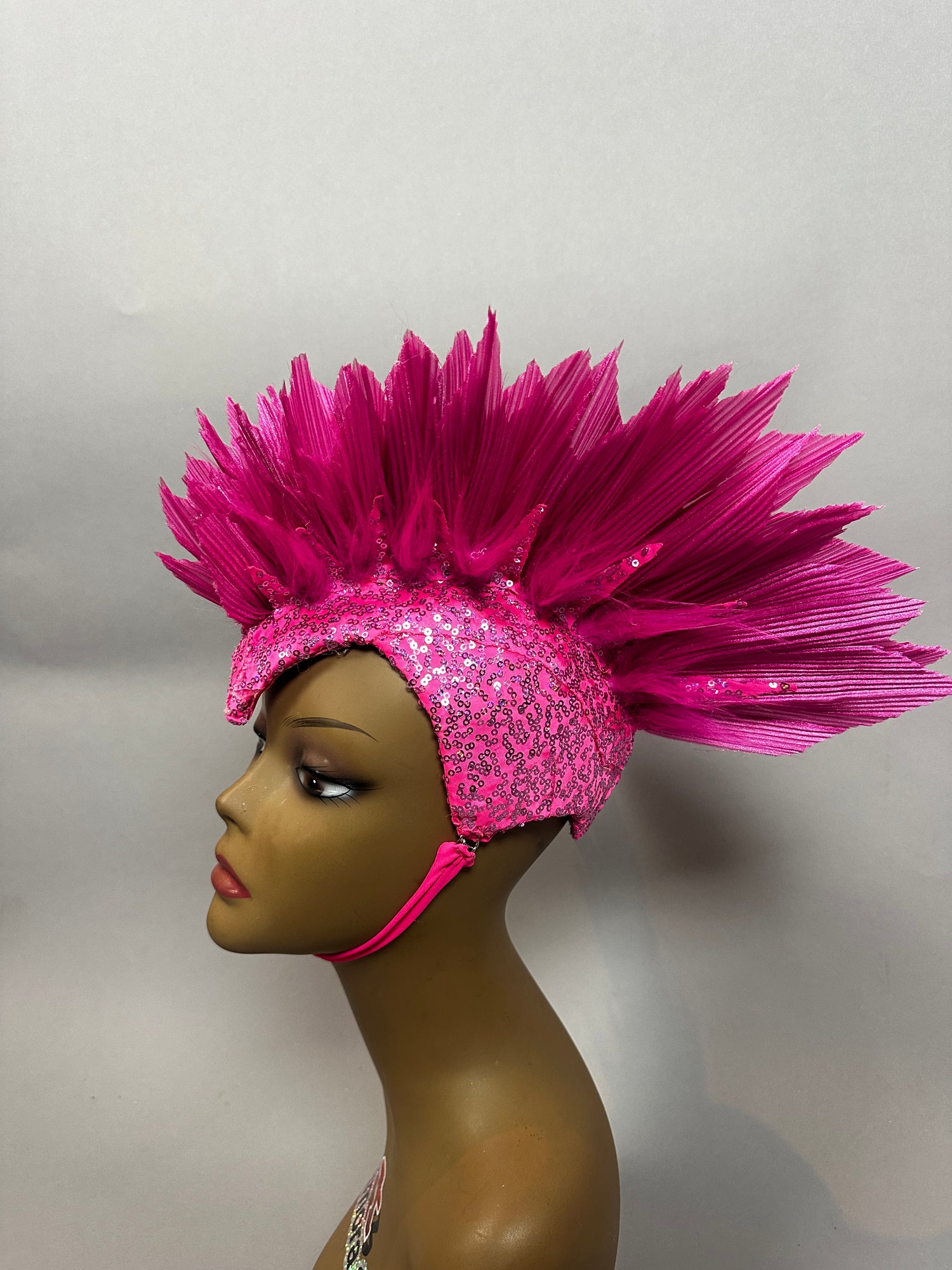A mannequin wears the Pink Bird Headpiece—a fairy hat with dramatic, spiked feather details—styled as theatrical headwear for an enchanting, aerialist-inspired look.