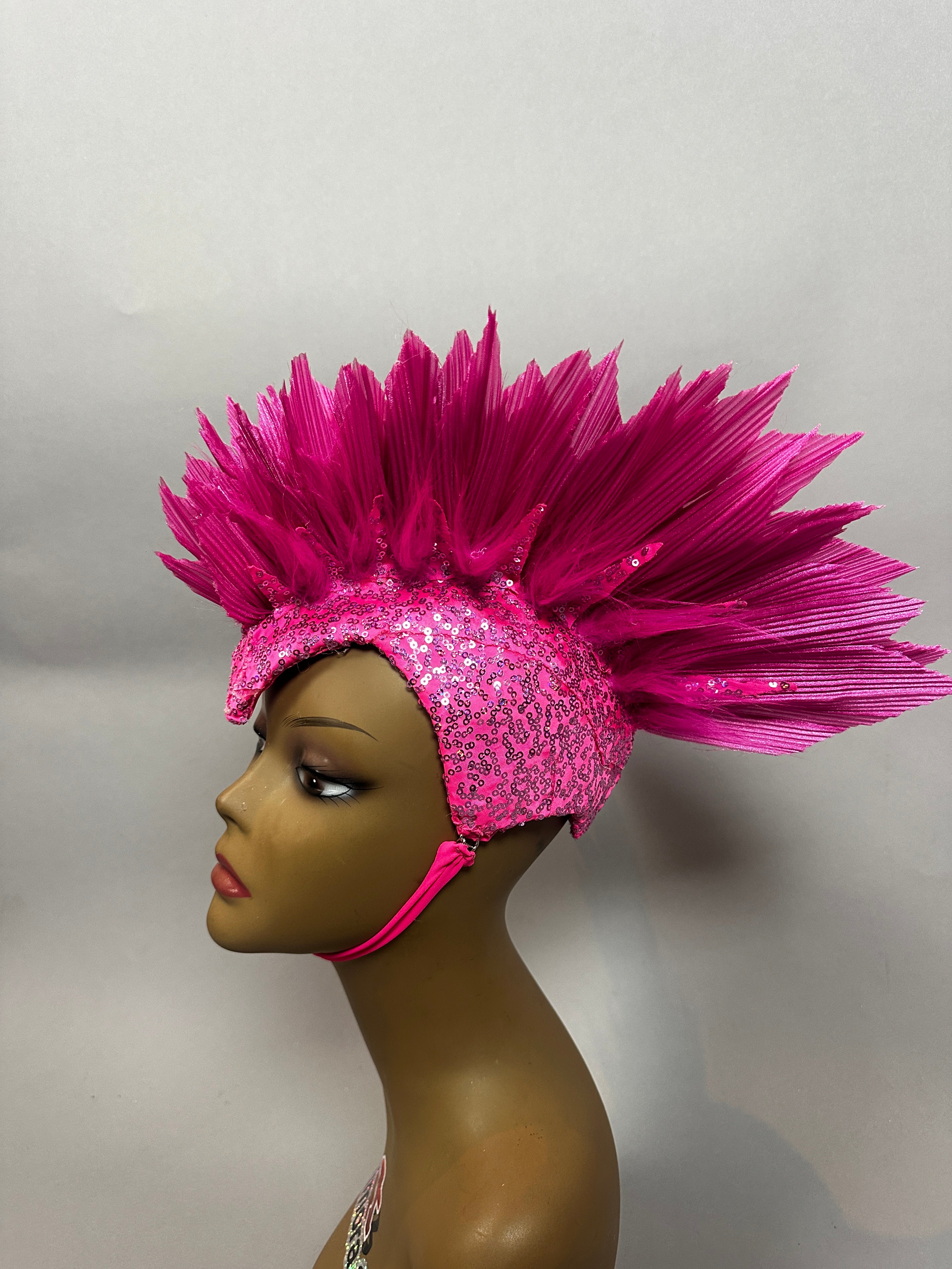 A mannequin wears the Pink Bird Headpiece—a fairy hat with dramatic, spiked feather details—styled as theatrical headwear for an enchanting, aerialist-inspired look.