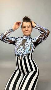 Woman in the Glamorous Sequins Stripes Catsuit costume, a black and white striped jumpsuit with blue ornate design, poses with hands near her head.