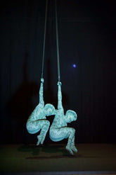 Two aerial performers wear custom-made Green Pixel Cobra snake print catsuits and headdresses, hanging upside down on straps against a dark background for a striking contortionist or serpent cosplay display.