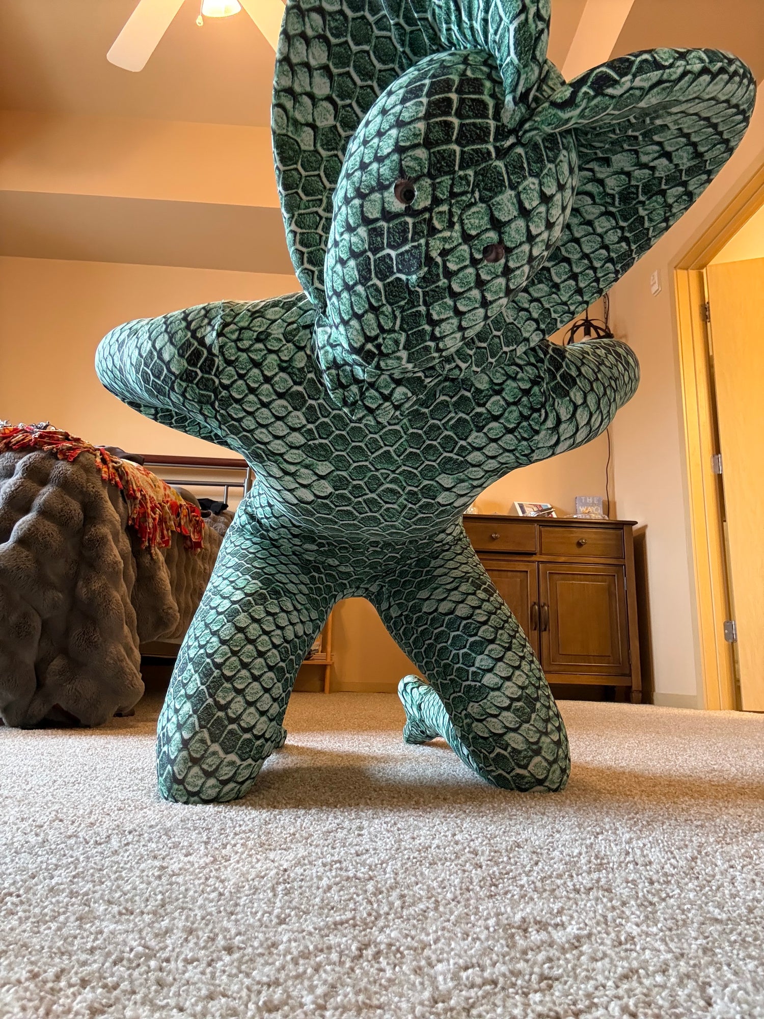 Person wearing a Green pixel Cobra Costume—snake print catsuit with headdress—kneeling on a bedroom carpet, resembling a reptilian creature.
