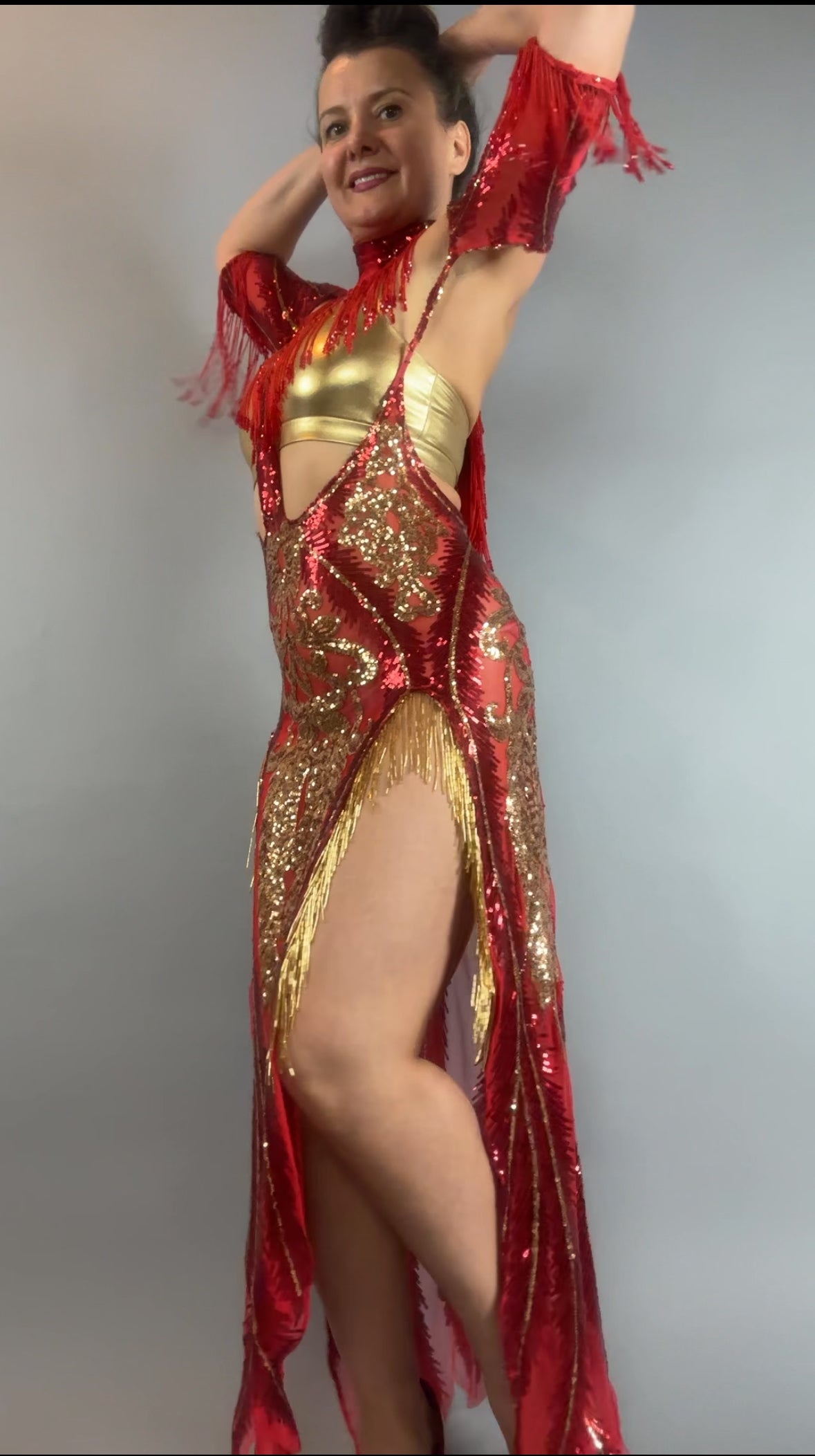 Model wears bearded French accessories’ Sequin Sheer Dress, a backless maxi with shimmering sequins and beaded fringe accessories, set against a plain background.