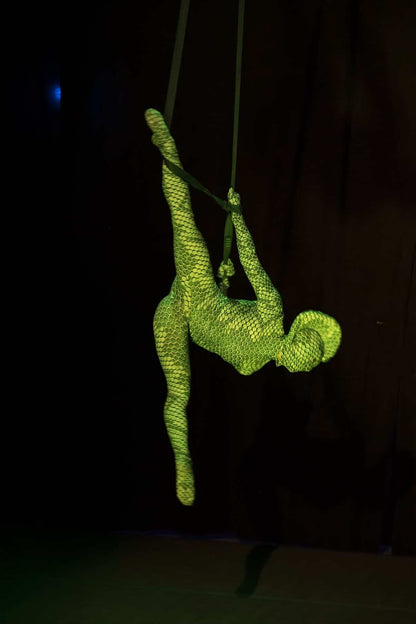 An aerialist in a Green pixel Cobra Costume Snake Print Catsuit contorts gracefully on suspended straps, the vibrant serpent cosplay and headdress creating a striking silhouette against the dark background.