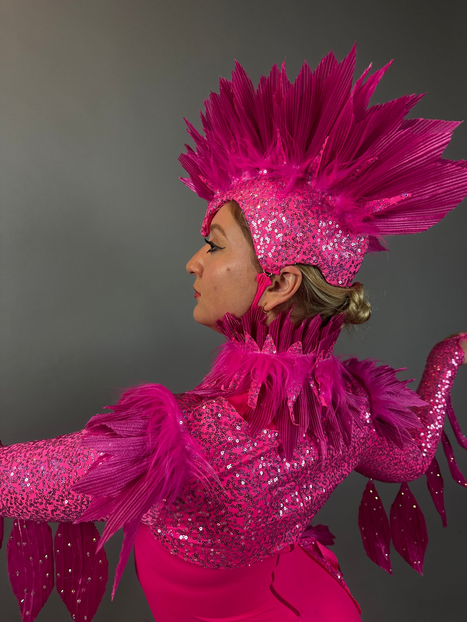 Model wears the Pink bird full costume for aerial and dancers, featuring bright pink feathers, sequins, and a dramatic headpiece, posing against a gray background.