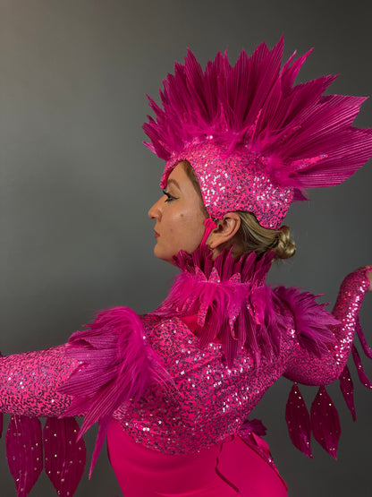Model wears the Pink bird full costume for aerial and dancers, featuring bright pink feathers, sequins, and a dramatic headpiece, posing against a gray background.