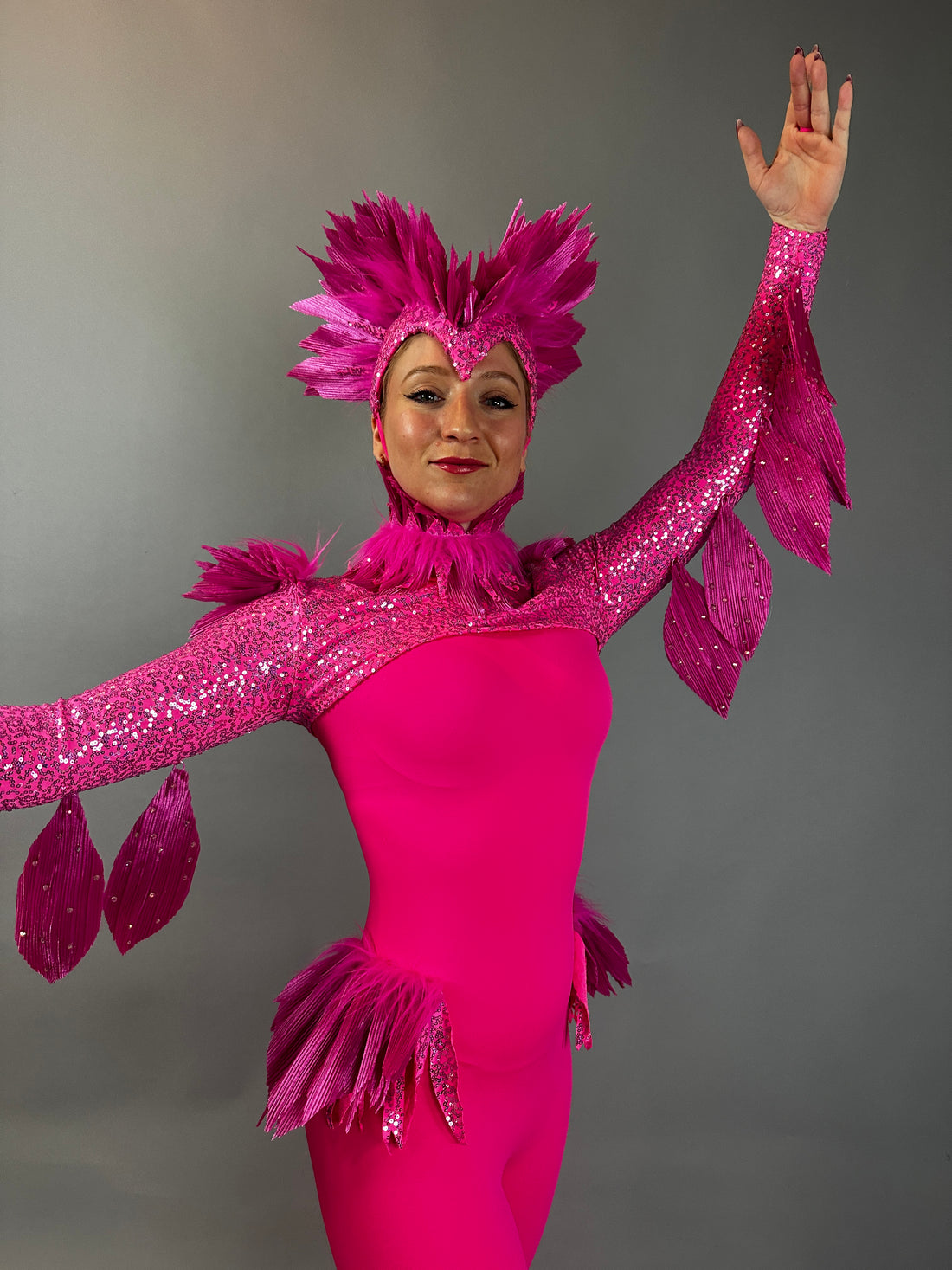 Person wearing the Pink bird full costume for aerial and dancers, featuring bright pink feathers and raised arms, stands against a plain gray background—ideal for stage performances or theatrical shows.