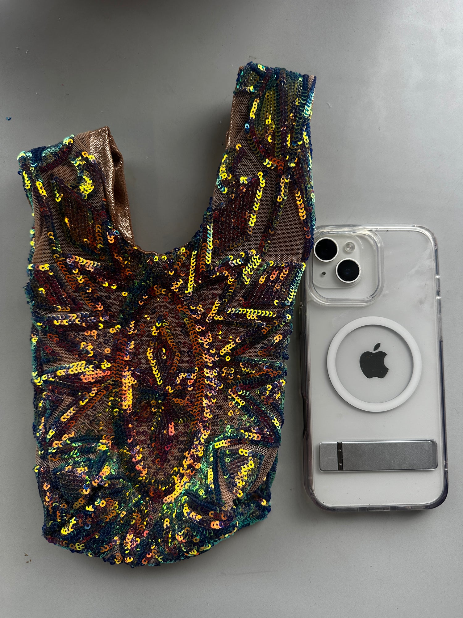 A Handcrafted reversible sequin mini tote, a sustainable fashion accessory, is placed beside a white iPhone with a clear case on a gray surface.