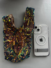 A Handcrafted reversible sequin mini tote, a sustainable fashion accessory, is placed beside a white iPhone with a clear case on a gray surface.