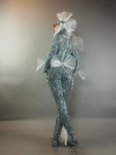 Model wears the Sea Creature costume—a shiny silver fish-scale bodysuit with translucent fin-like accents—posing against a gray background and highlighting avant-garde, couture-inspired design.