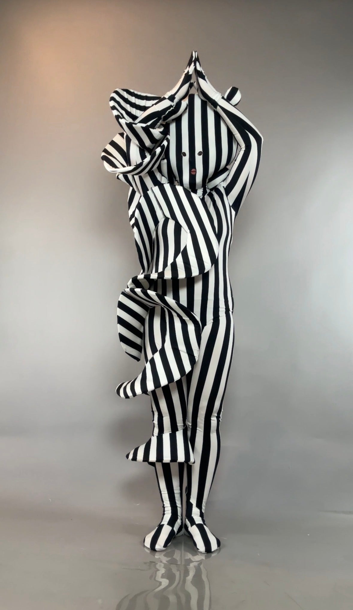 Person in a Black and White Striped Creature Costume with Sculptural Details, featuring large ruffles and a face mask.