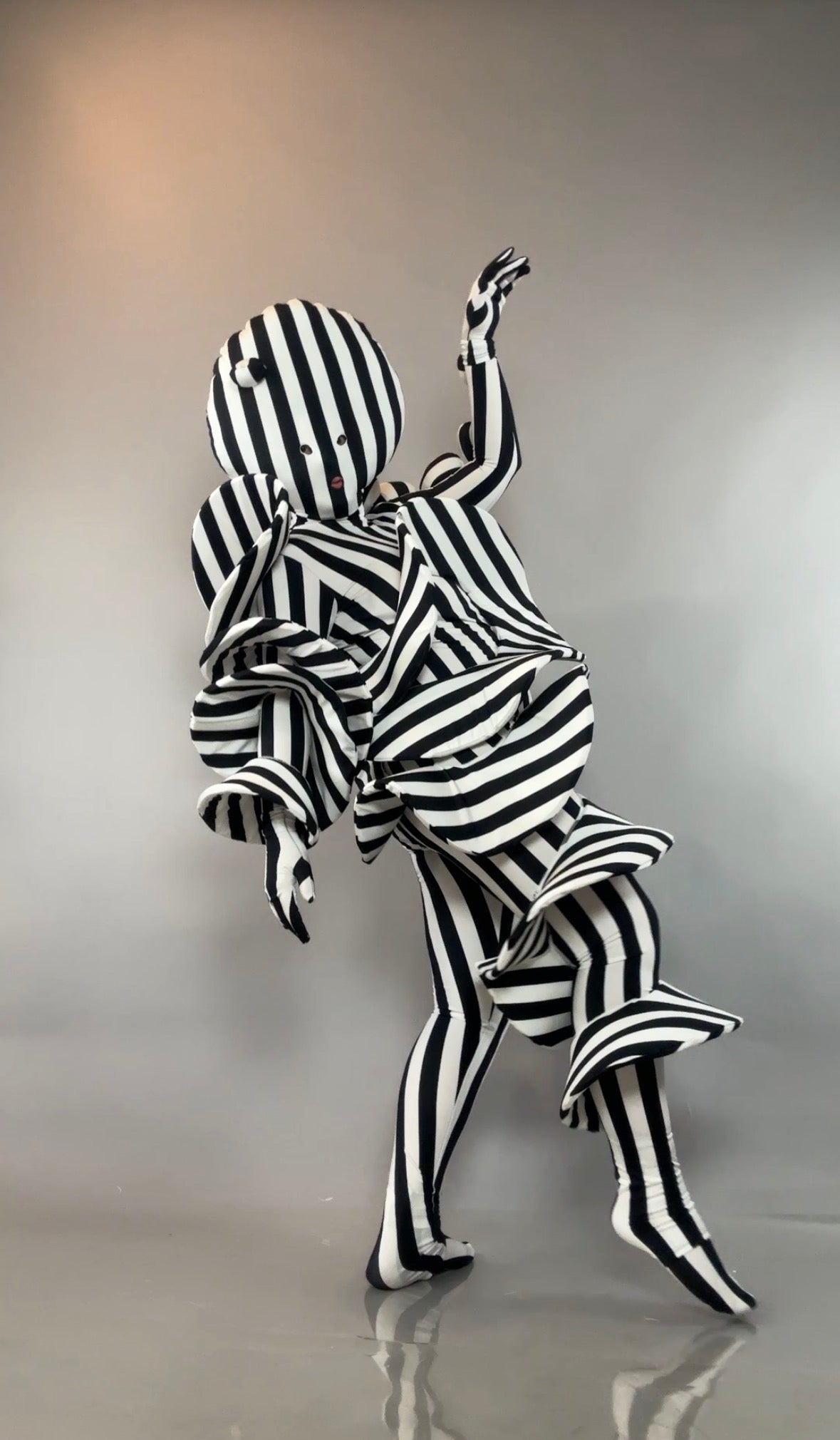 A person in a Black and White Striped Creature Costume with sculptural, ruffled layers.