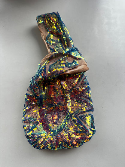 Handcrafted reversible sequin mini tote—a colorful, sustainable fashion accessory with a looped handle—lies on a light gray surface.