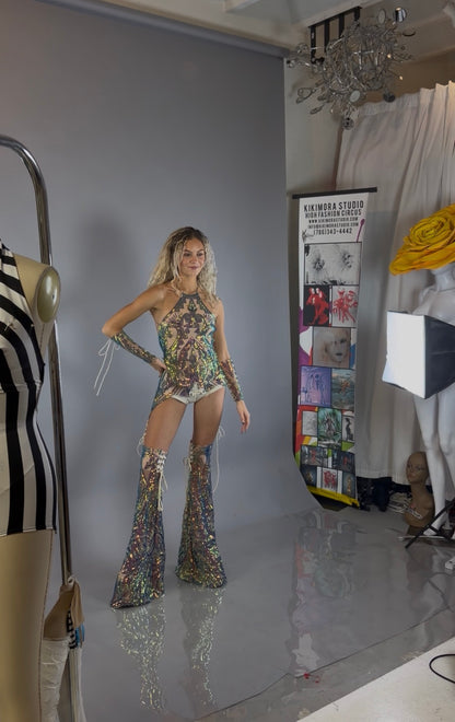 A model showcases a stunning custom dancewear look in a vibrant sequins costume set, featuring chaps pants and a laced top designed as a festival costume, photographed in a fashion studio.