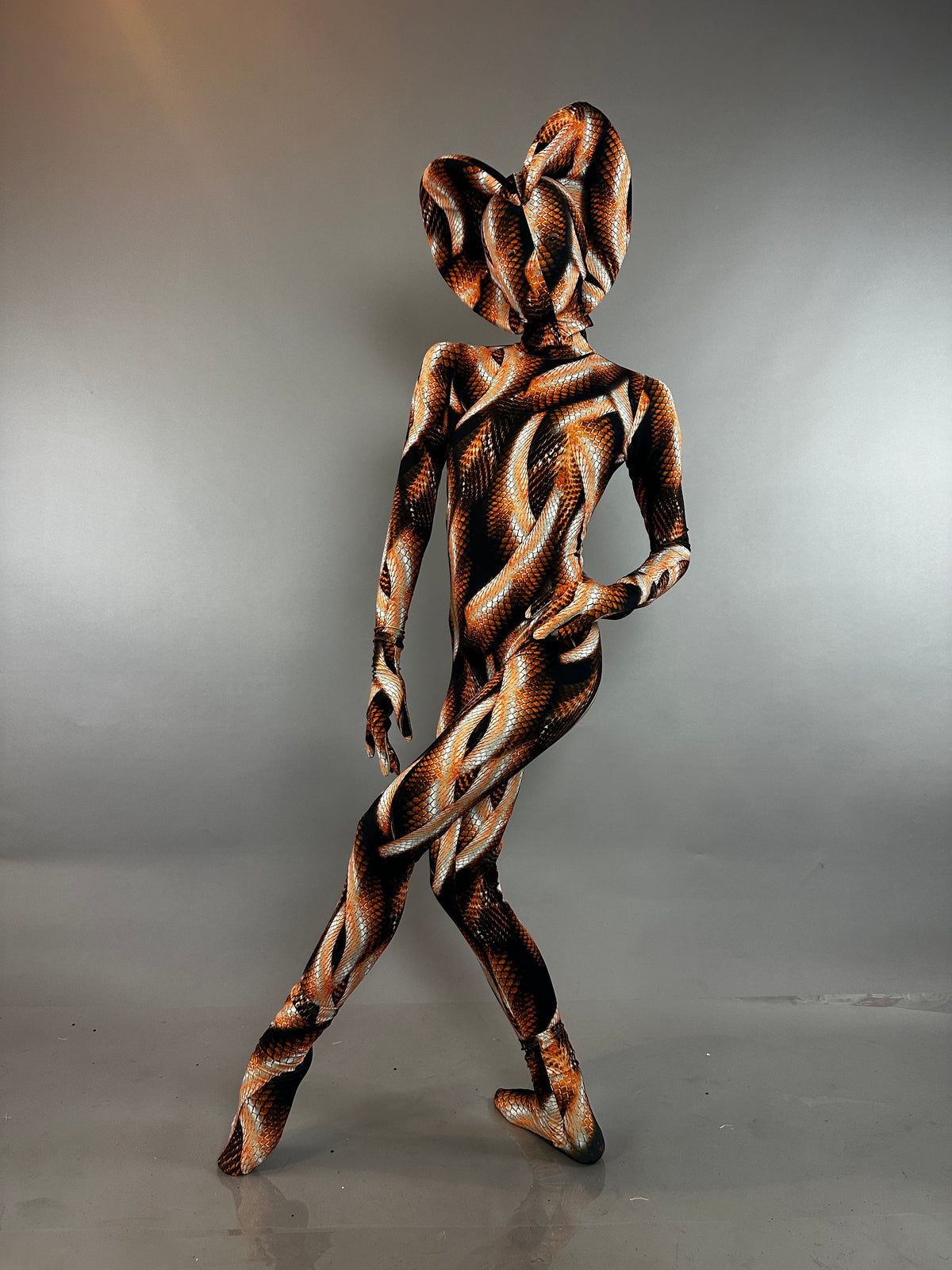 Person wearing a Brown Snake Print Turtleneck Catsuit with Back Zipper and matching headpiece in orange and brown.