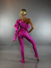 Model wears the Ruffle Catsuit—an asymmetrical, one-shoulder spandex jumpsuit in bright pink—posing against a plain gray background.