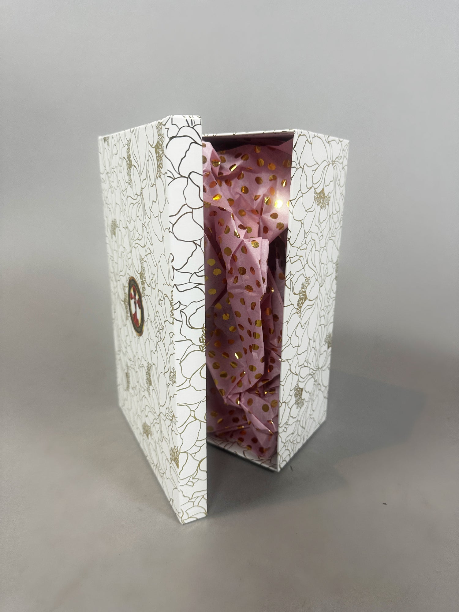 White floral-patterned box partly open, showing pink tissue paper with gold dots—perfect for gifting the Mini Living Rose sculpture doll ornament or other art from Kikimora Studio.
