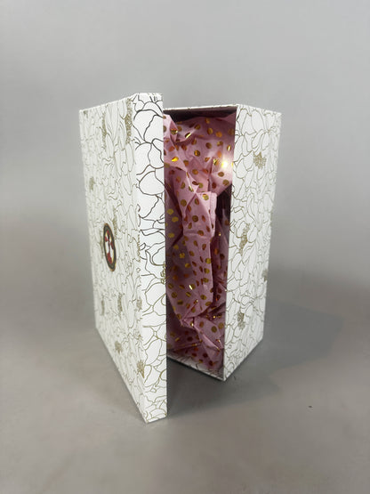 White floral-patterned box partly open, showing pink tissue paper with gold dots—perfect for gifting the Mini Living Rose sculpture doll ornament or other art from Kikimora Studio.