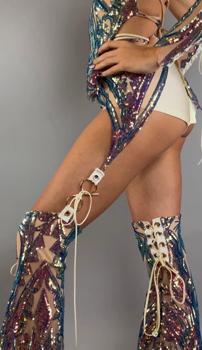 Woman wearing a sparkling sequin festival costume set, featuring chaps pants and a laced top with white briefs, posing against a gray background.