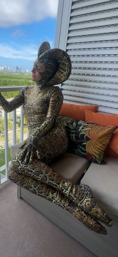 Wearing the Green Cobra Snake Costume, a person poses on a balcony couch with colorful pillows. This custom-made outfit is perfect for gymnasts, acrobats, dancers, and contortionists.