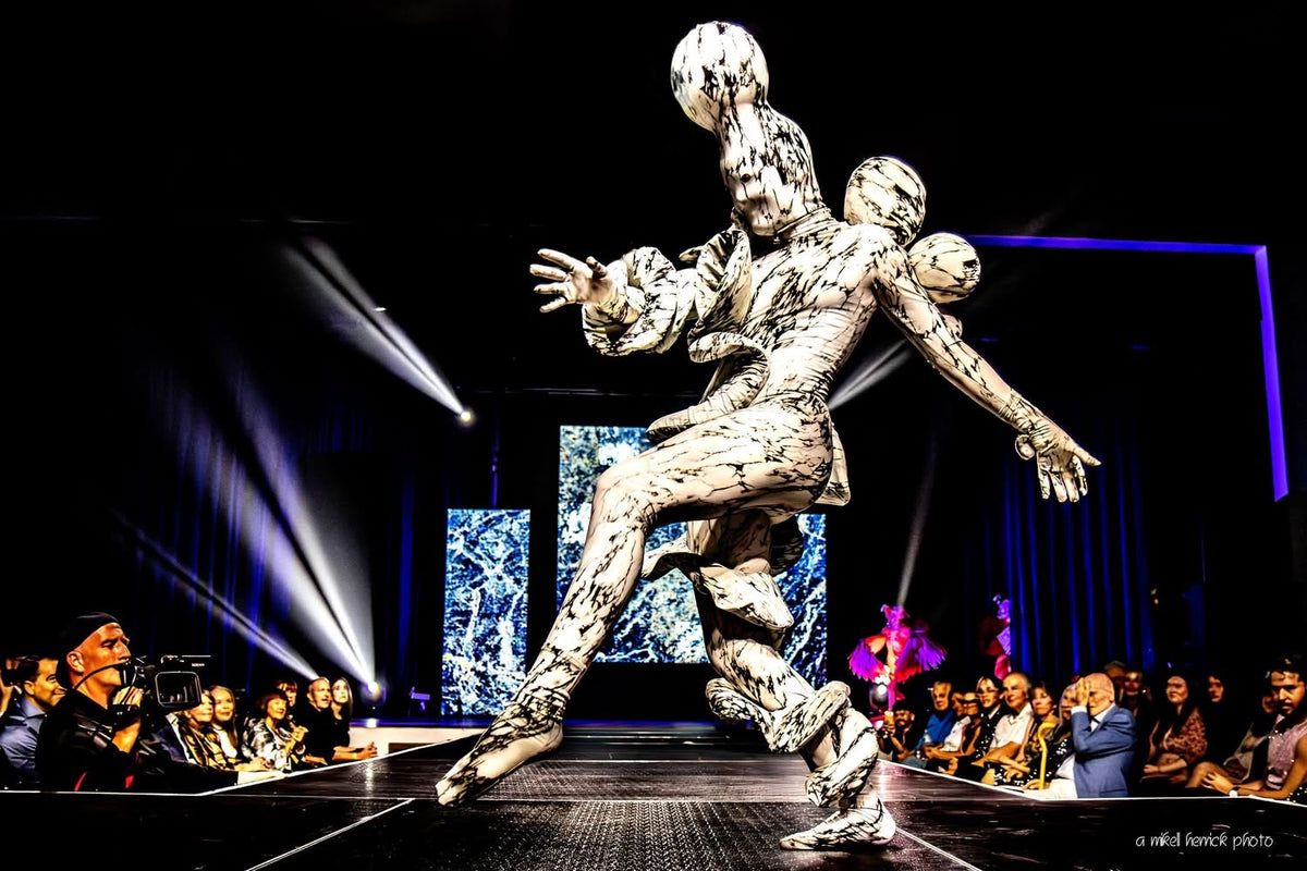 A performer in a Mush­room Creature Costume—an avant-garde full body suit with marble print spandex and striking abstract design—glides down the runway, captivating the audience under stage lights with its UV glow and artistic fungus-inspired details.