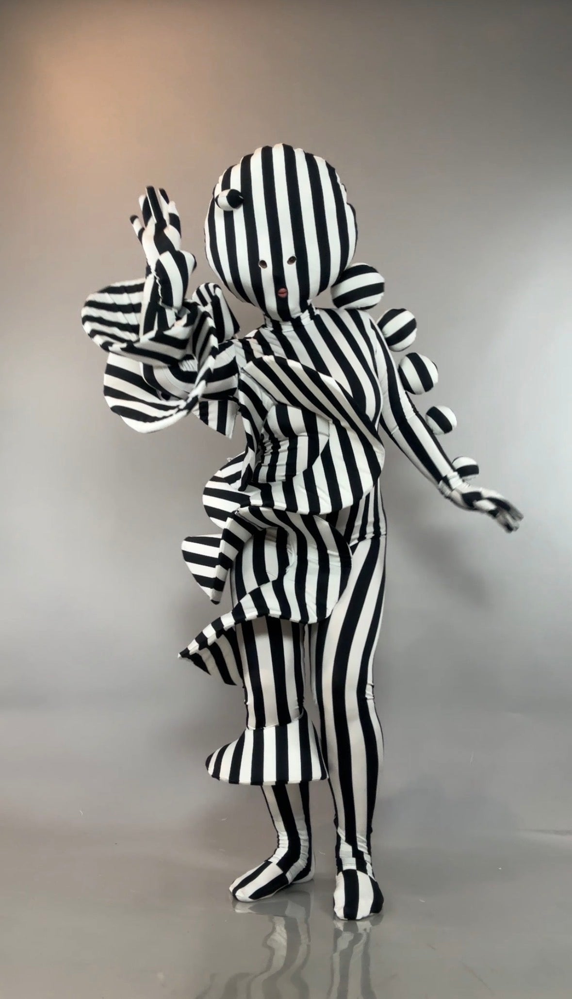 Person in a Black and White Striped Creature Costume with Sculptural Details, featuring ruffles and spherical accents.