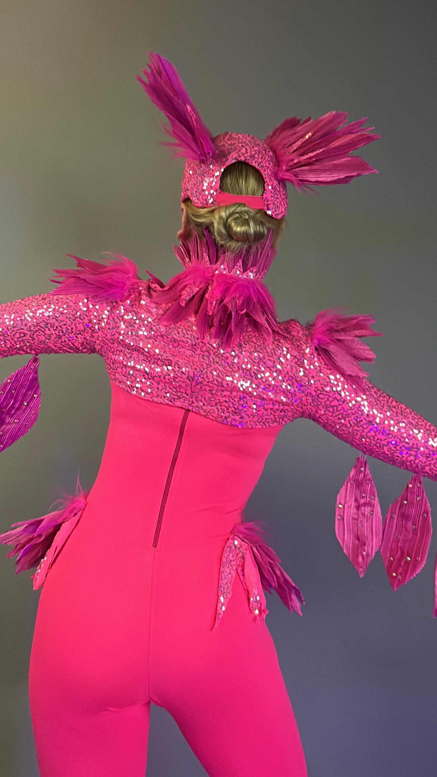 Person in the Pink Bird Full Costume for Aerial and Dancers—vivid pink, sparkling, with feathers and outstretched wings—faces away from the camera, perfect for dazzling stage performances.