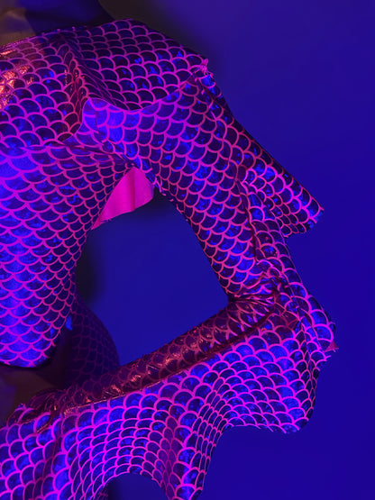 A person wears the Red Ruffle Catsuit featuring an off-shoulder spandex design and asymmetrical ruffles, posing against a blue background.