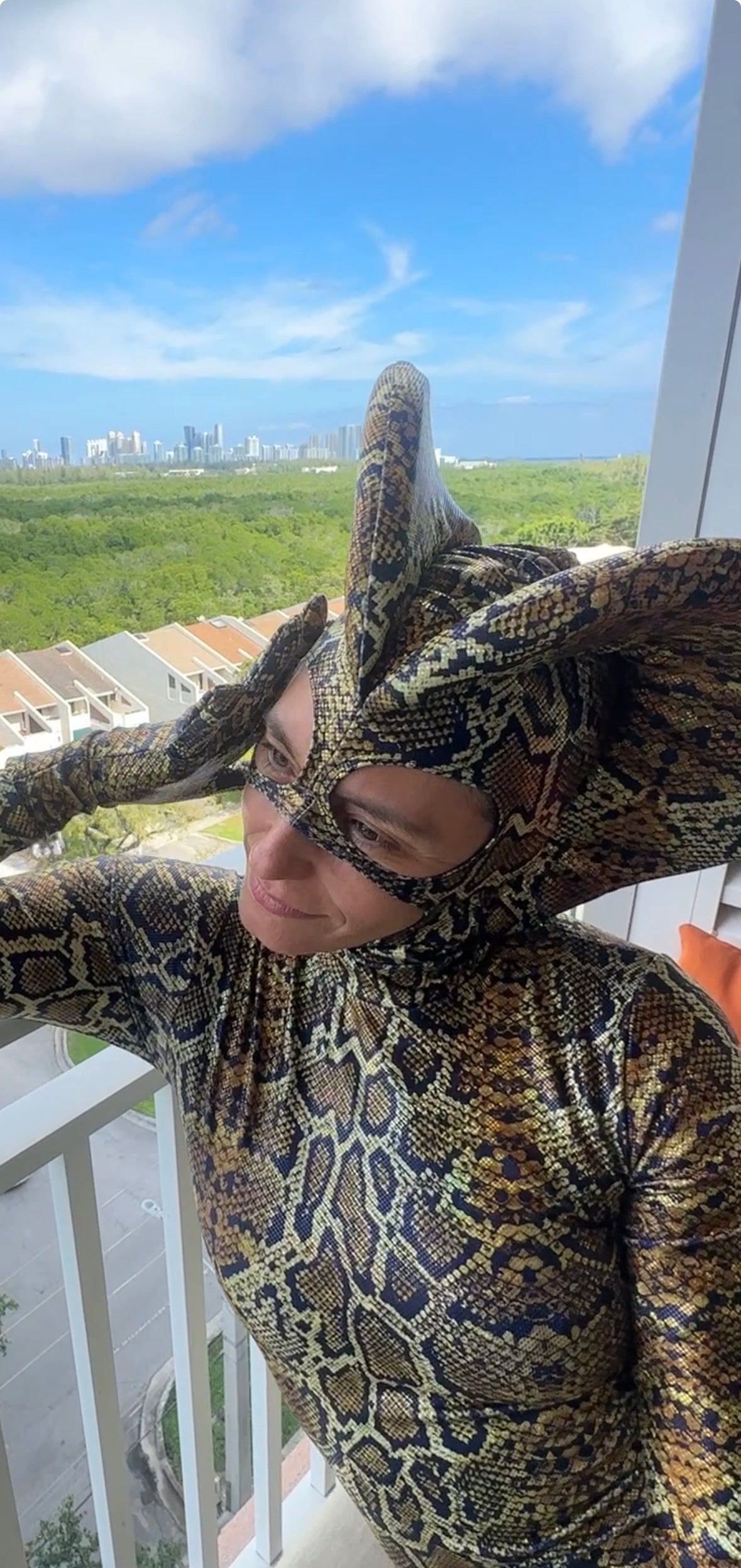 Wearing the custom Green Cobra Snake Costume, a person in a shiny spandex catsuit with a dramatic snake headpiece stands on a balcony, overlooking the city—perfect for gymnastics, acrobatics, dancers, and contortionists.