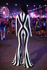 At a festival, someone wears the Rave White Striped Catsuit with bellbottom legs, standing out amid vibrant lights and a glowing ferris wheel—a bold performer outfit.