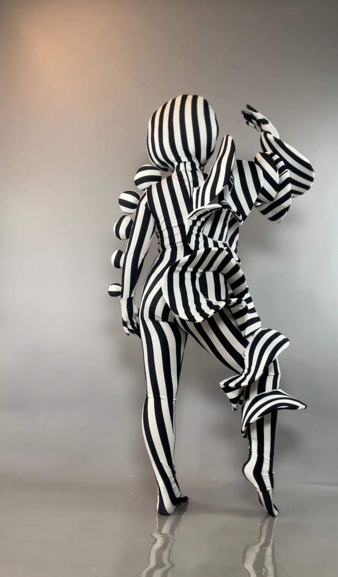Person in a Black and White Striped Creature Costume with large, sculptural circular and pleated accents.