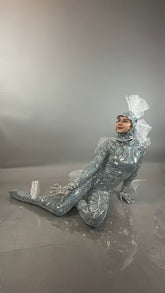 Model in the Sea Creature bodysuit with an elaborate headpiece poses seated on the floor against a gray backdrop, capturing the striking allure of couture-inspired design.