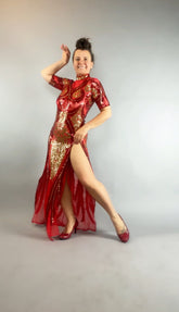 Woman wears a Red and Gold Sequin Sheer Dress, sleeveless, with hand accessories, posing with one leg raised and smiling against a plain light background.