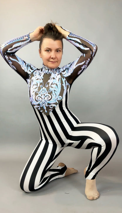Person kneeling in the Glamorous sequins Stripes Catsuit costume, featuring black-and-white stripes, blue patterns, and a sequined leaf design, hands holding hair, on a gray background.