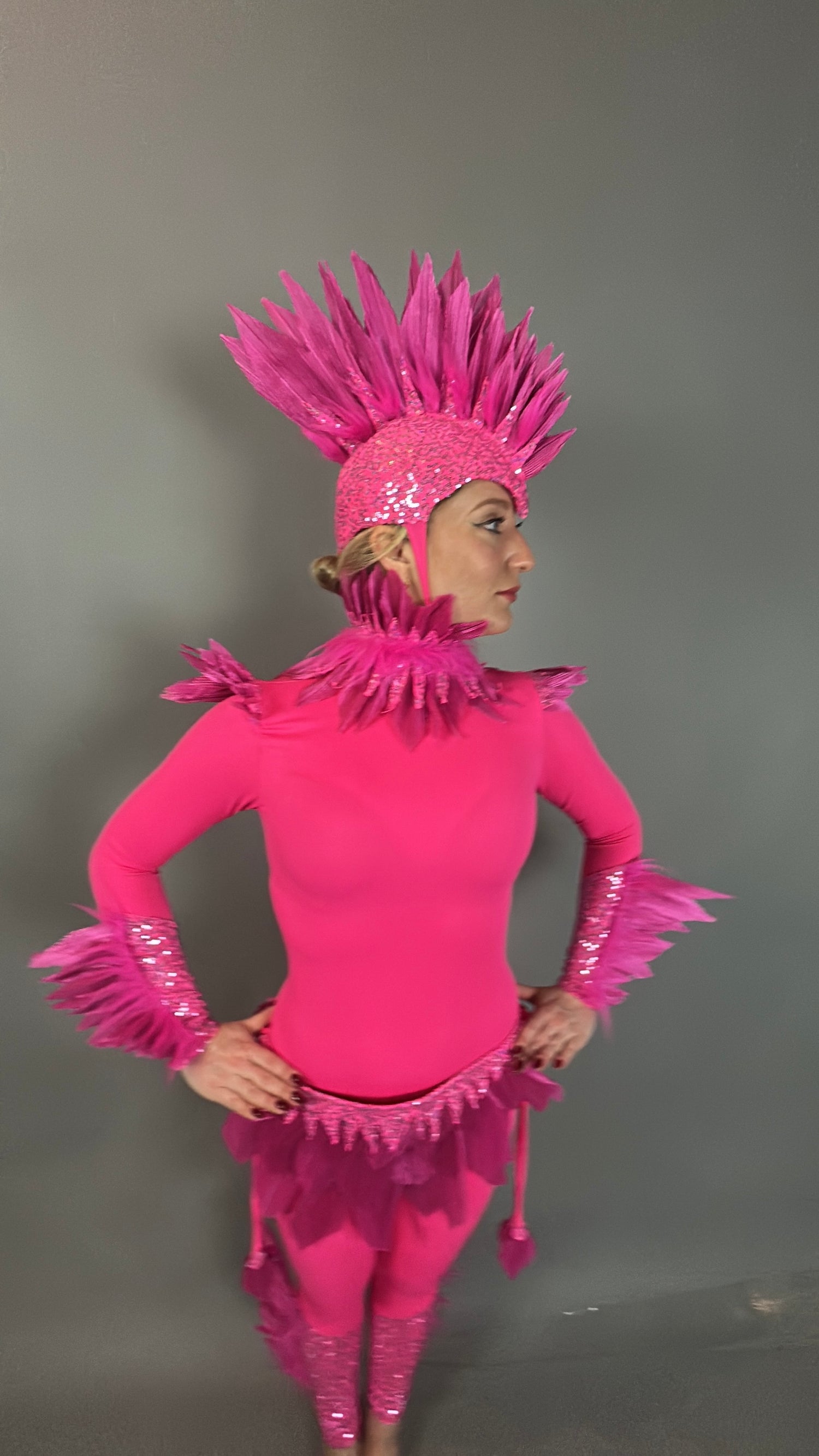 Person wearing the Pink Bird Headpiece, a fairy hat accessory with feathered accents, styled as aerialist headwear and theatrical costume prop, standing against a plain gray background.