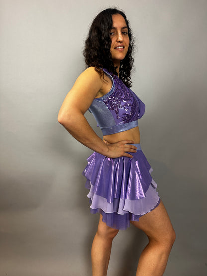 A woman poses sideways against a plain gray background, modeling the Lavender Purple Sequin Dance Costume featuring a crop top, high waist shorts with a half skirt, and 4-way stretch mesh—an eye-catching fire dancer outfit.