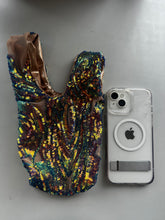 A handcrafted, reversible sequin mini tote—a sustainable fashion accessory—rests beside a clear iPhone with a MagSafe ring on a gray surface.