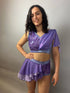 A woman poses slightly smiling in a Lavender Purple Sequin Dance Costume—featuring high waist shorts with a half skirt, crop top, and 4-way stretch mesh—against a plain light background.