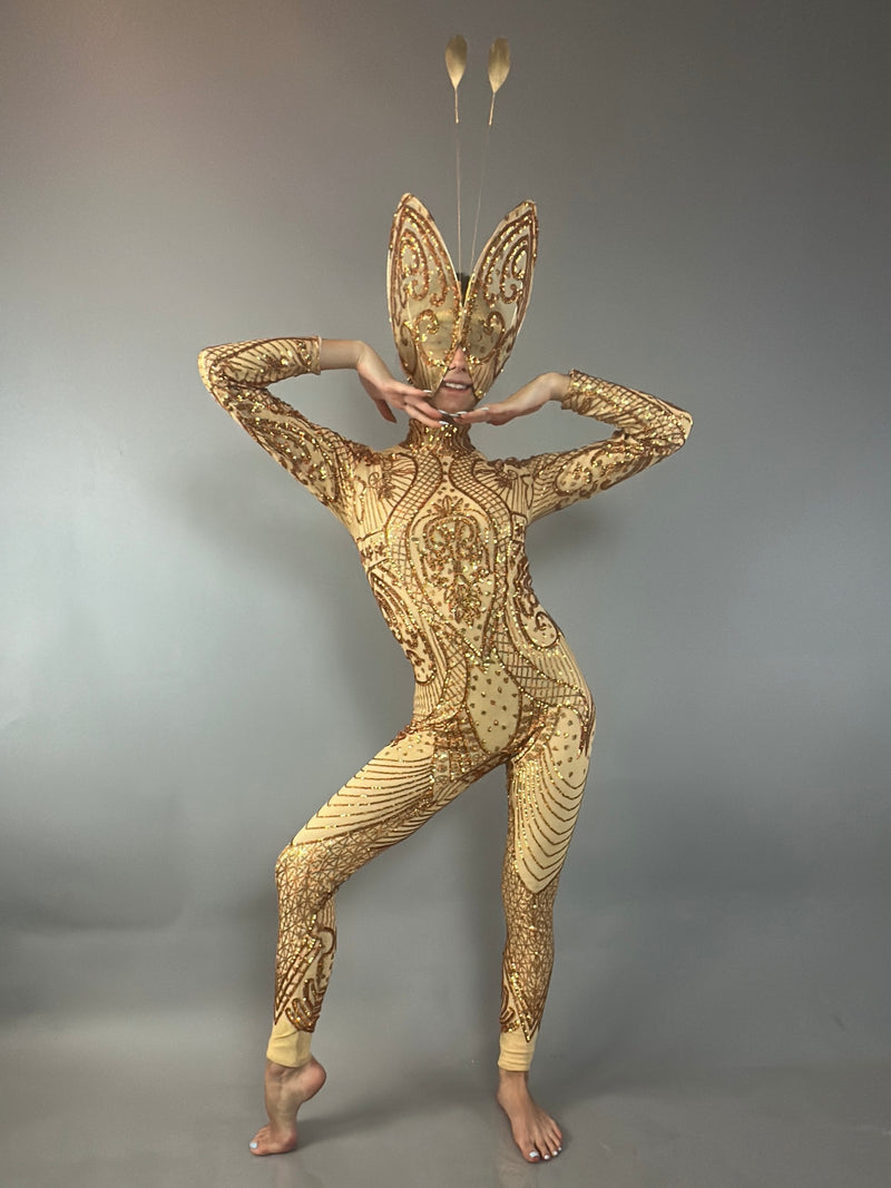 Person in a gold, ornate bodysuit and butterfly headpiece poses with arms framing their face against a gray background, showcasing the dazzling Golden Butterfly Sparkling Sequin Full Costume—an ideal addition to any performance costume collection.