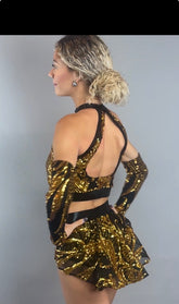 A woman models the Gold Sequin on Black Crop Top and Bottom Set, featuring a halterneck top and hand accessories. She poses sideways with hands on hips against a plain background, while touches of black mesh accentuate the shimmering golden sequins for a striking look.