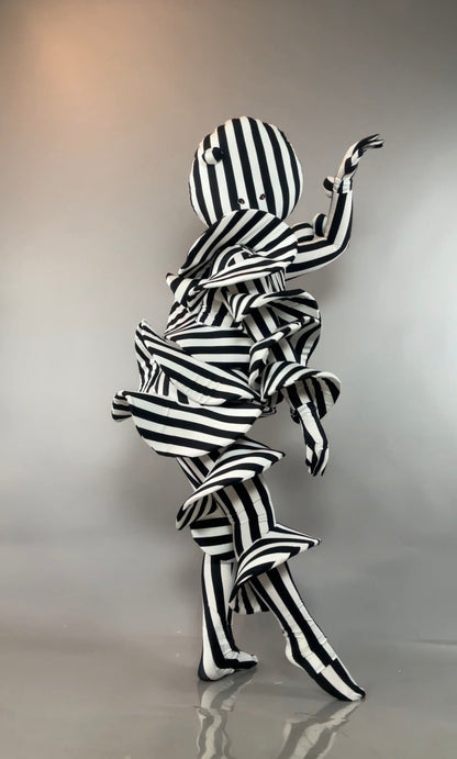 A person in a Black and White Striped Creature Costume featuring a rounded headpiece and sculptural, ruffled layers.