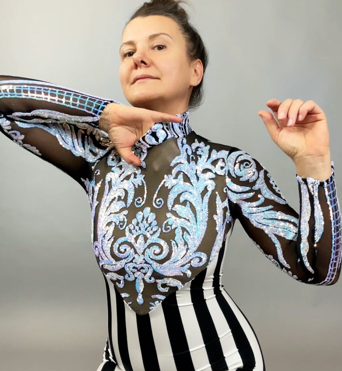 Wearing the Glamorous Sequins Stripes Catsuit, this person poses with arms raised, showcasing its iridescent green fabric and striking leaf-inspired sequin design against a plain backdrop.