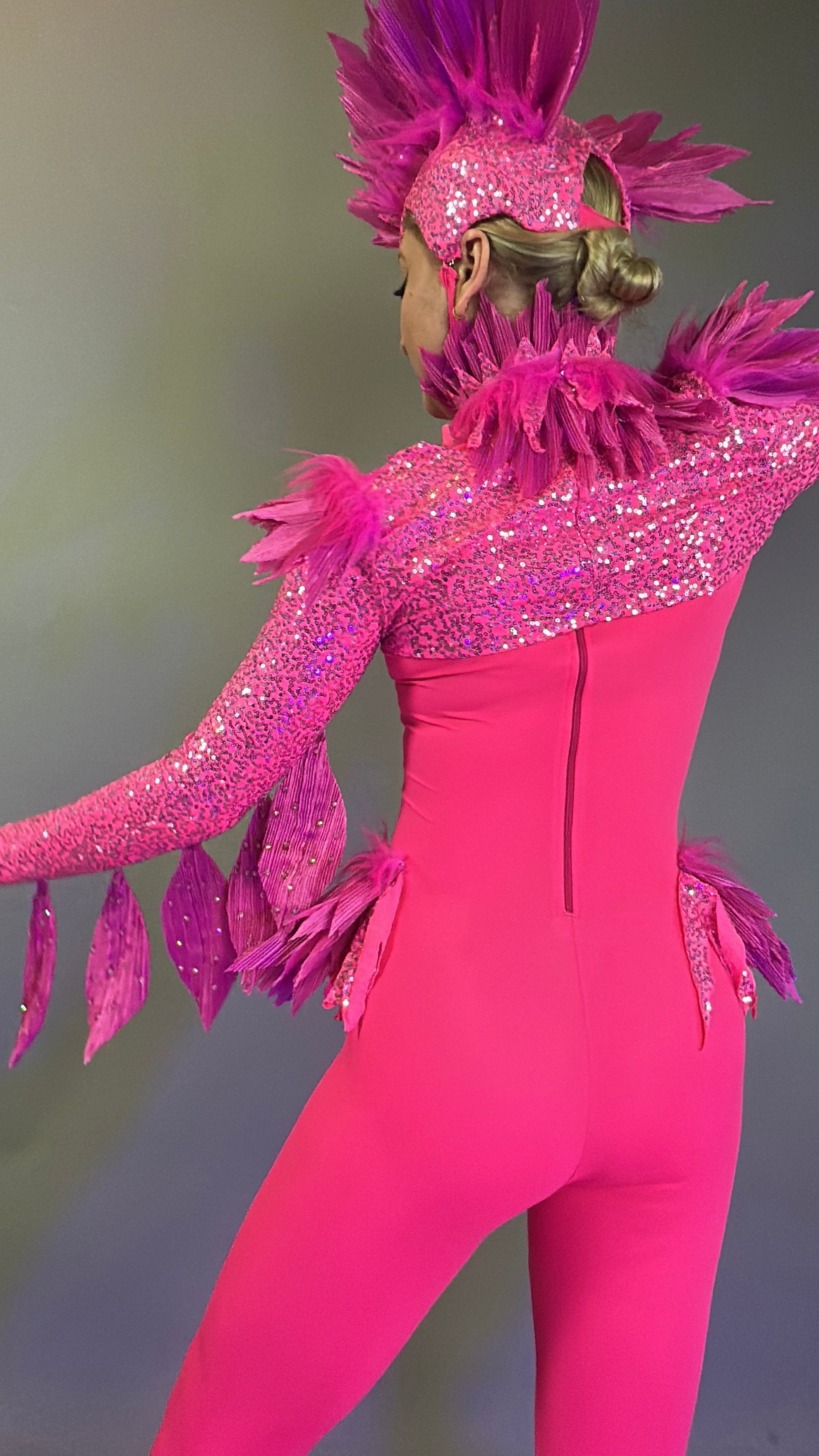 Person wearing the Pink bird full costume for aerial and dancers, featuring bright pink feathers and sparkly details, with headpiece, shown from the back against a plain background.