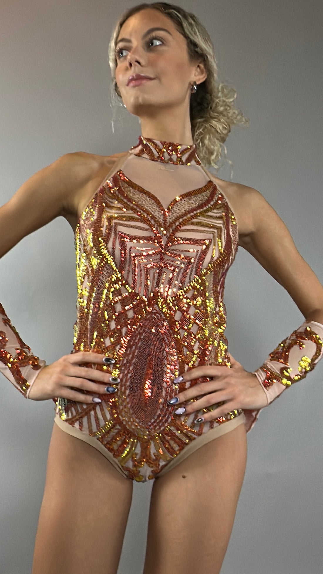 A model poses confidently against a plain gray background wearing the Fire color sparkling Halter Leotard with sequin accents and detachable sleeves.