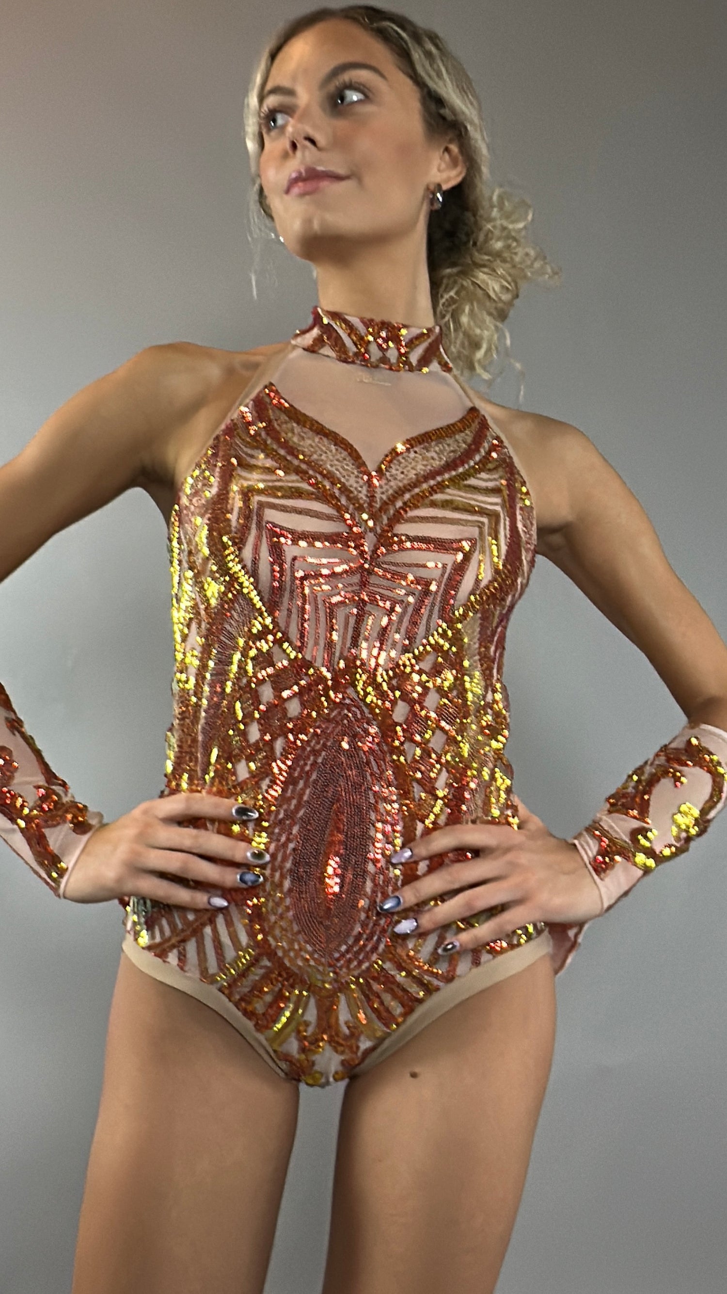 A model poses confidently against a plain gray background wearing the Fire color sparkling Halter Leotard with sequin accents and detachable sleeves.