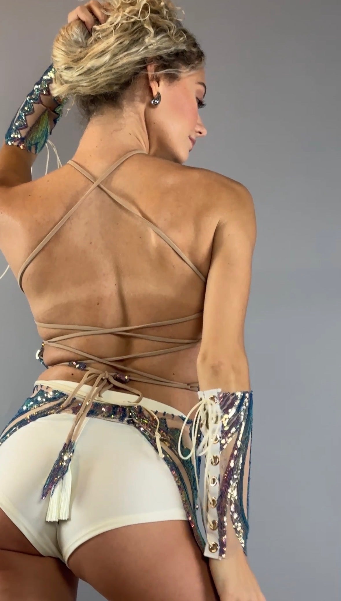 A woman poses with her back to the camera against a plain background, wearing the Chaps pants and laced top festival costume set adorned with sequins.