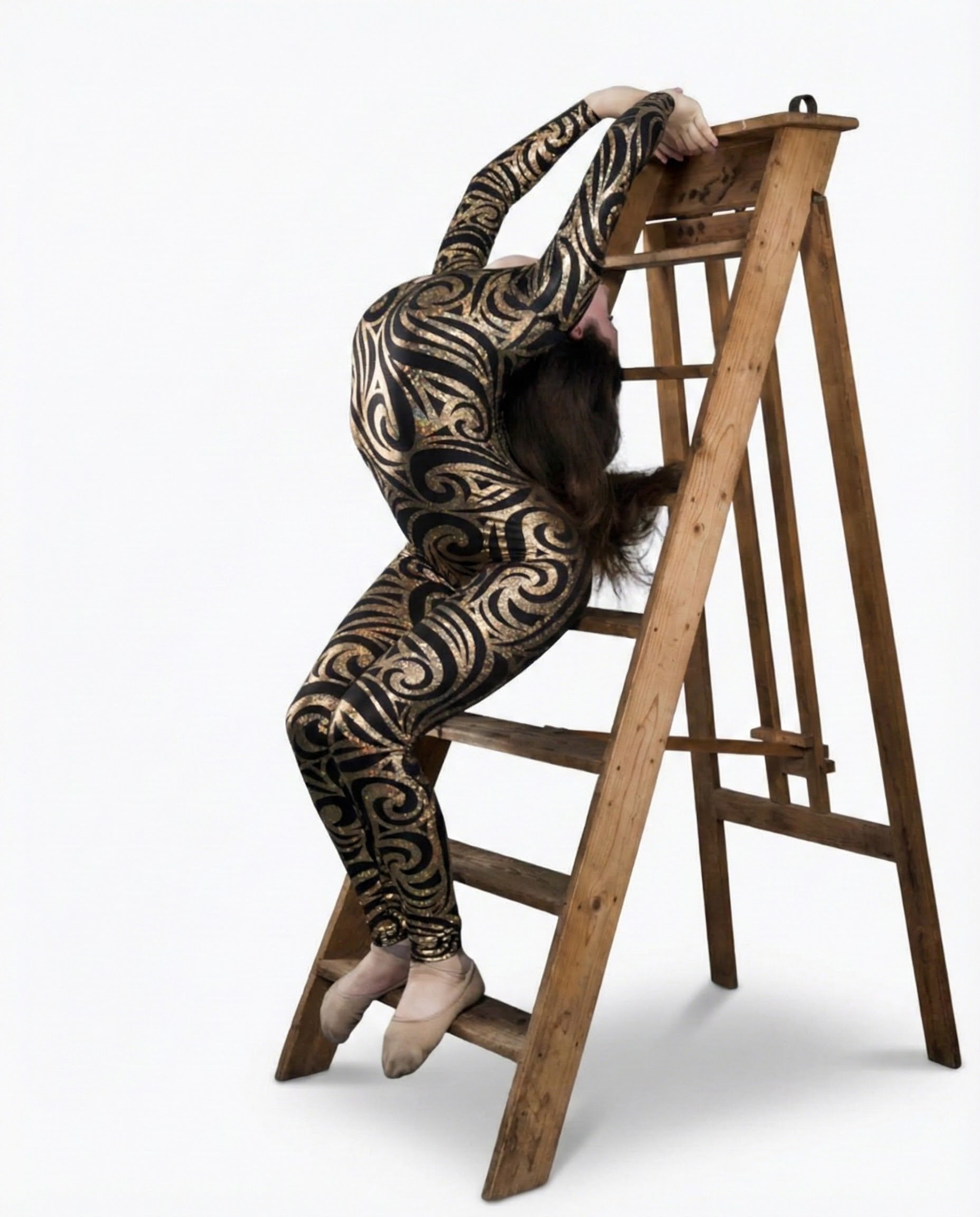 A contortionist in a Black Swirl On Holographic Catsuit with a scoop neck and full sleeves bends backward over a wooden stepladder.