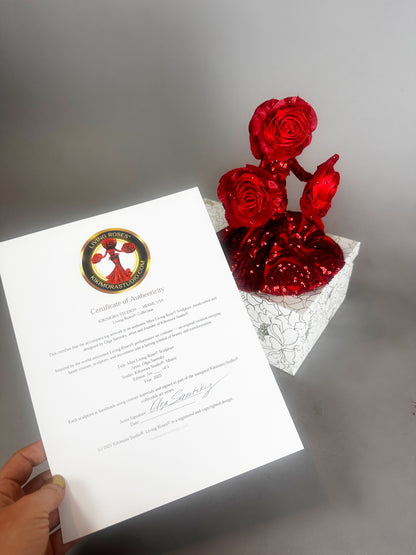 A hand holds a certificate beside a white box with three Mini Living Rose sculptures—doll ornaments by Kikimora Studio, each handcrafted and sparkling with red glitter.