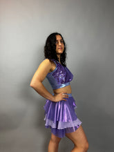 A model poses confidently in the Lavender Purple Sequin Dance Costume—featuring a crop top, high waist shorts with half skirt, and 4-way stretch mesh—against a plain gray background.